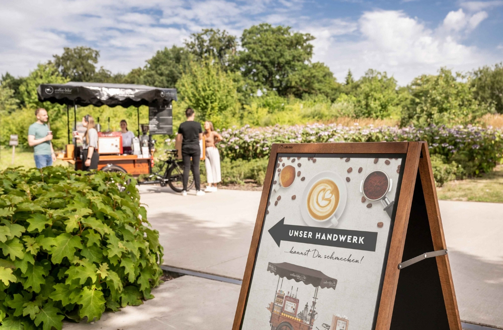 Hinweisschild deutet auf den Kaffeeverkauf vom Coffee-Bike links hin