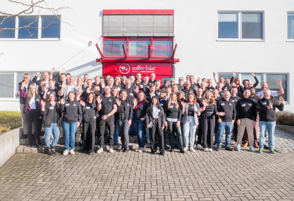 Coffee-Bike employees and franchise partners stand in front of the Coffee-Bike headquarters waving