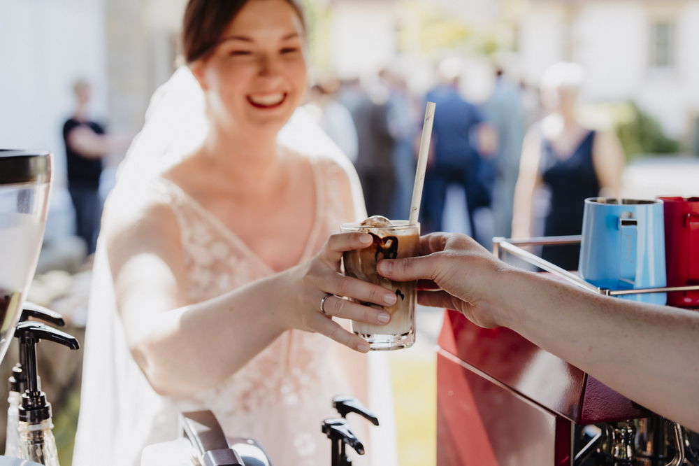 Coffee-Bike Hochzeitscatering. Braut hält Iced Latte in der Hand. Barista reicht ihr ihn an.