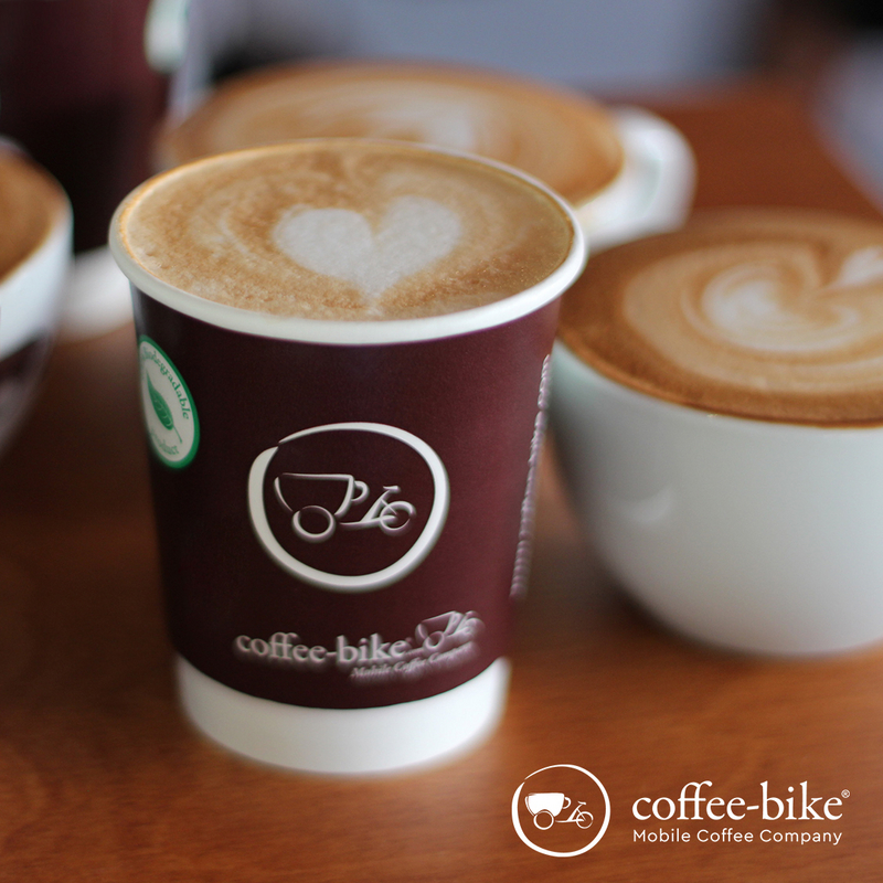 Coffee-Bike disposable cup with heart latte art and next to it white cup with latte art, bottom right white Coffee-Bike logo