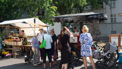 Six customers stand in front of the Coffee-Bike, next to it a stand with flowers