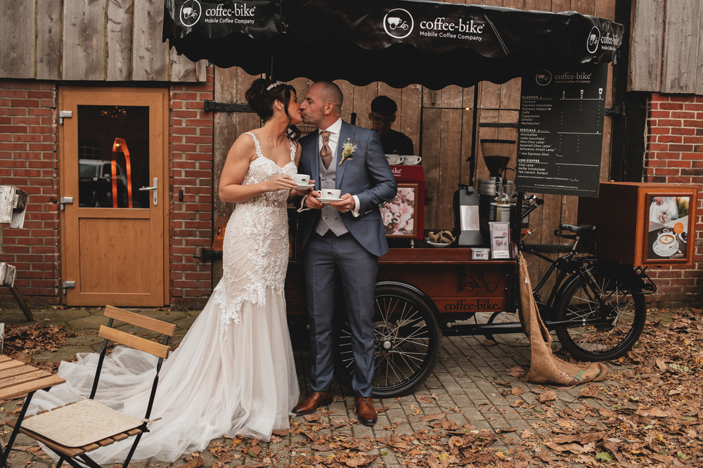 Hochzeitspaar steht vor dem Coffee-Bike und küsst sich. 