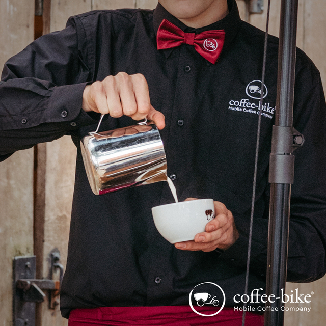 Coffee-Bike Barista gießt Milch in eine Kaffeetasse