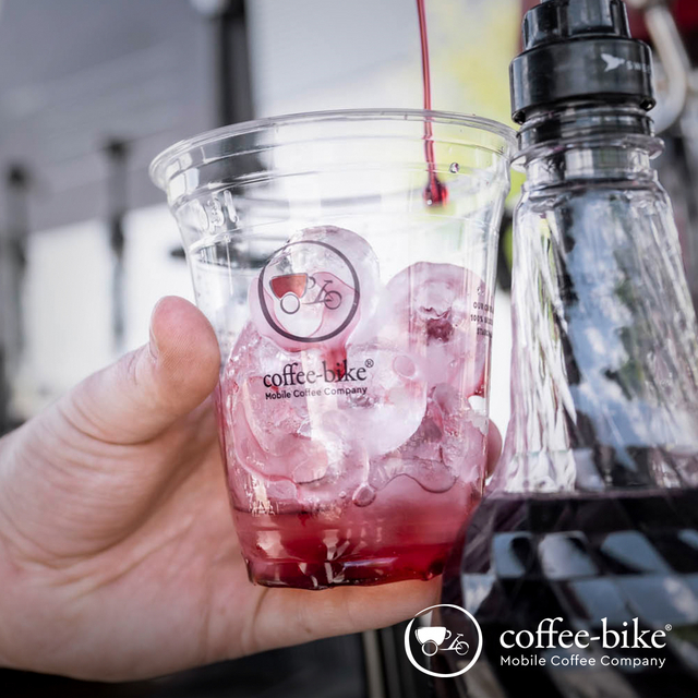 Hand hält durchsichtigen Becher mit Coffee-Bike Logo und rotem Inhalt