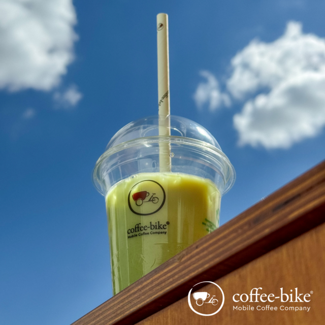 Iced matcha latte in a coffee bike cup against a blue sky