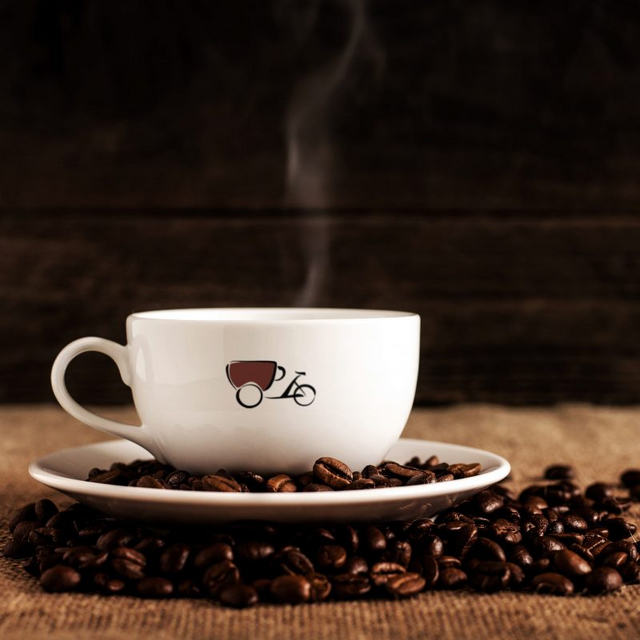 Frontansicht auf Weiße Coffee-Bike Tasse mit Untertasse, die auf verstreuten Bohnen steht.