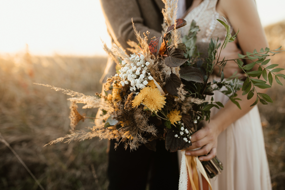 Hochzeitspaar hält Blumenstrauß in der Hand.