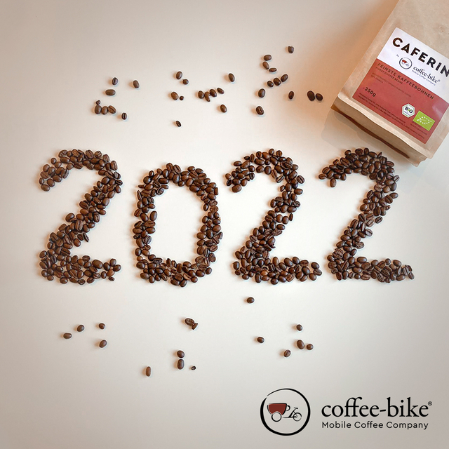 Auf einem hellen Hintergrund liegen Bohnen in Form einer 2022, oben rechts liegt eine Caferino Kaffeepackung und unten rechts das Coffee-Bike Logo