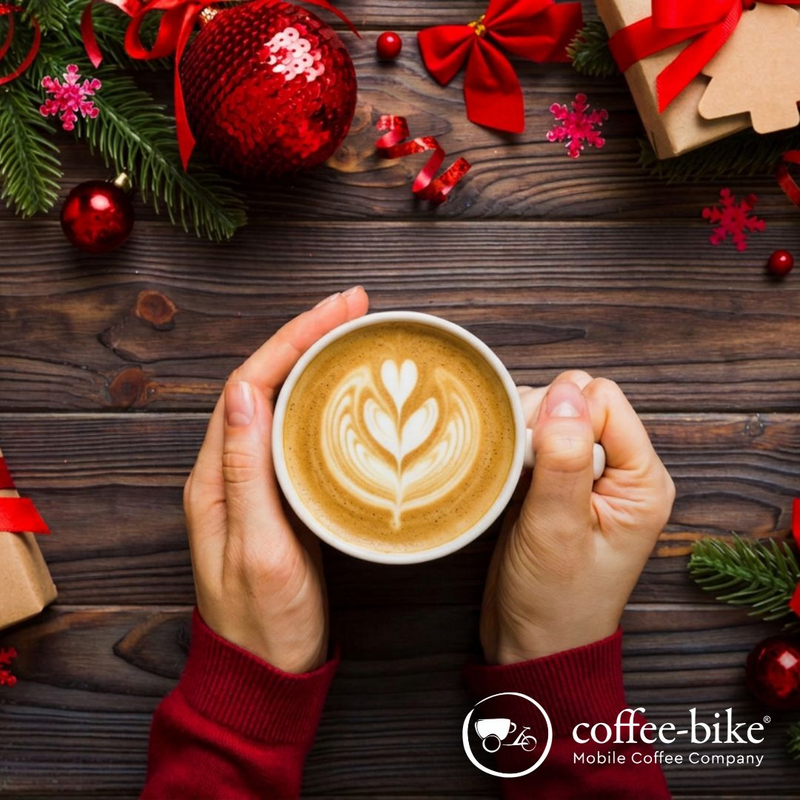 Hände halten Tasse mit Latte Art und Weihnachtsdeko im Hintergrund