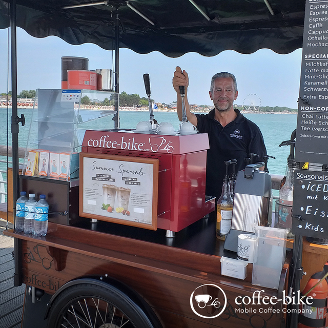 Man pulling the lever of the Coffee-Bike portafilter machine, in the background sea