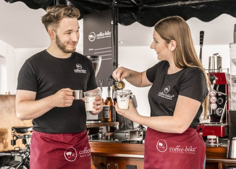 Coffee-Bike Barista Training mit einem Barista und einer Barista, die am Coffee-Bike gemeinsam Kaffee zubereiten