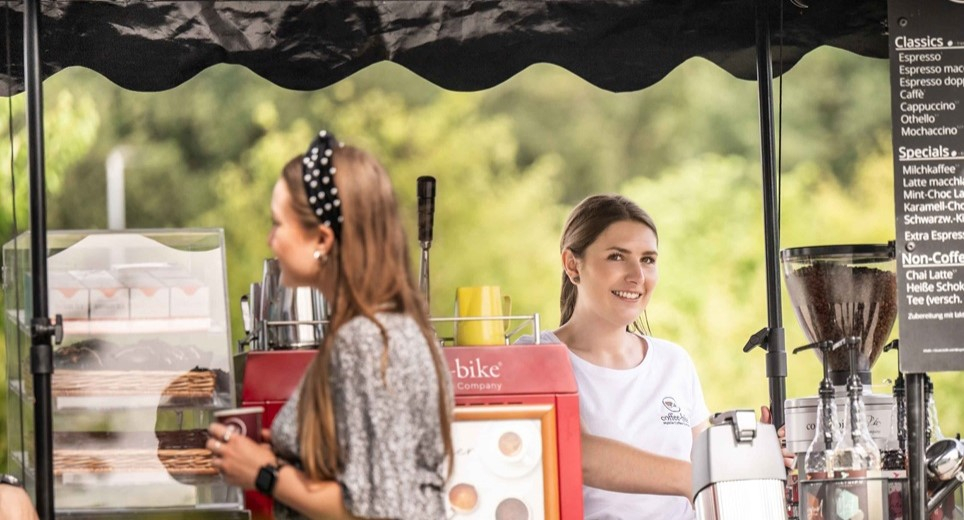 Coffee-Bikerin bedient an dem mobilen Kaffeefahrrad eine Kundin