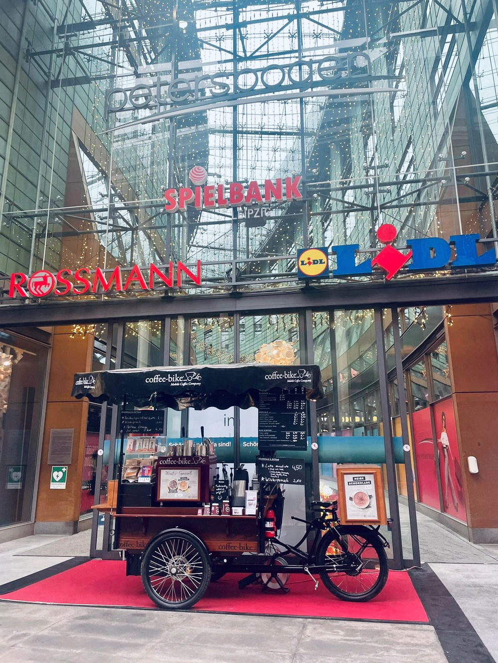 Ein vollausgestattetes Coffee-Bike steht auf einem roten Teppich vor einem Einkaufszentrum