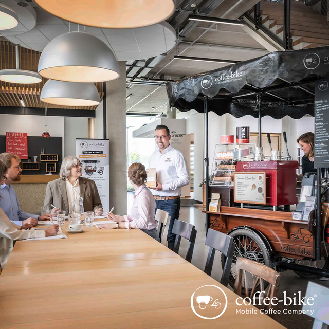 [Translate to UK:] On the right side a Coffee-Bike with barista and on the left side people at the table