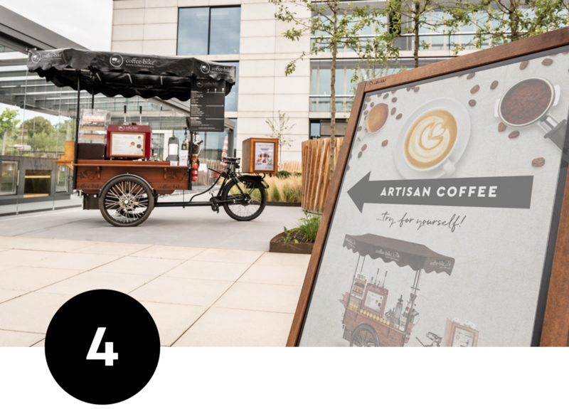 În fața unui sediu de companie, Coffee-Bike este gata de vânzare, pe fundalul unui opritor de client care indică locul de vânzare.