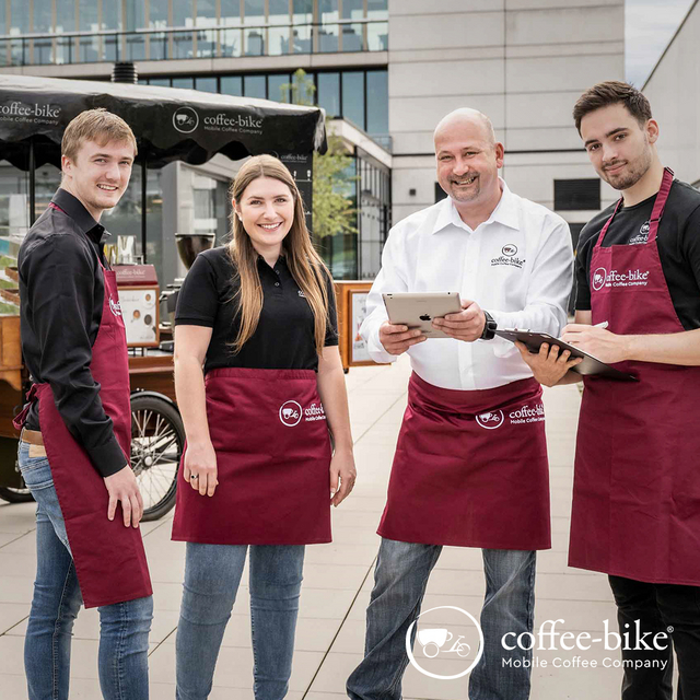 Drei Männer und eine Frau in Coffee-Bike Kleidung stehen vor dem Coffee-Bike