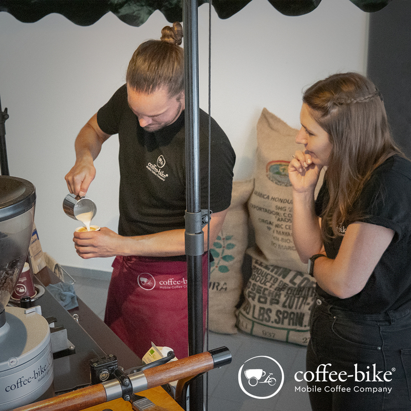 A woman watches a Coffee-Bike barista pour milk into a cup