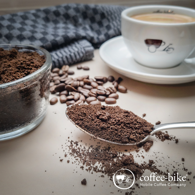 Coffee powder on a spoon, behind it Coffee-Bike cup and blue towel