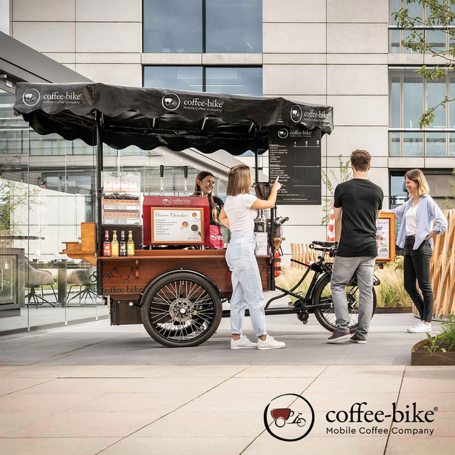 Ein Coffee-Bike mit Barista und drei Personen drumherum