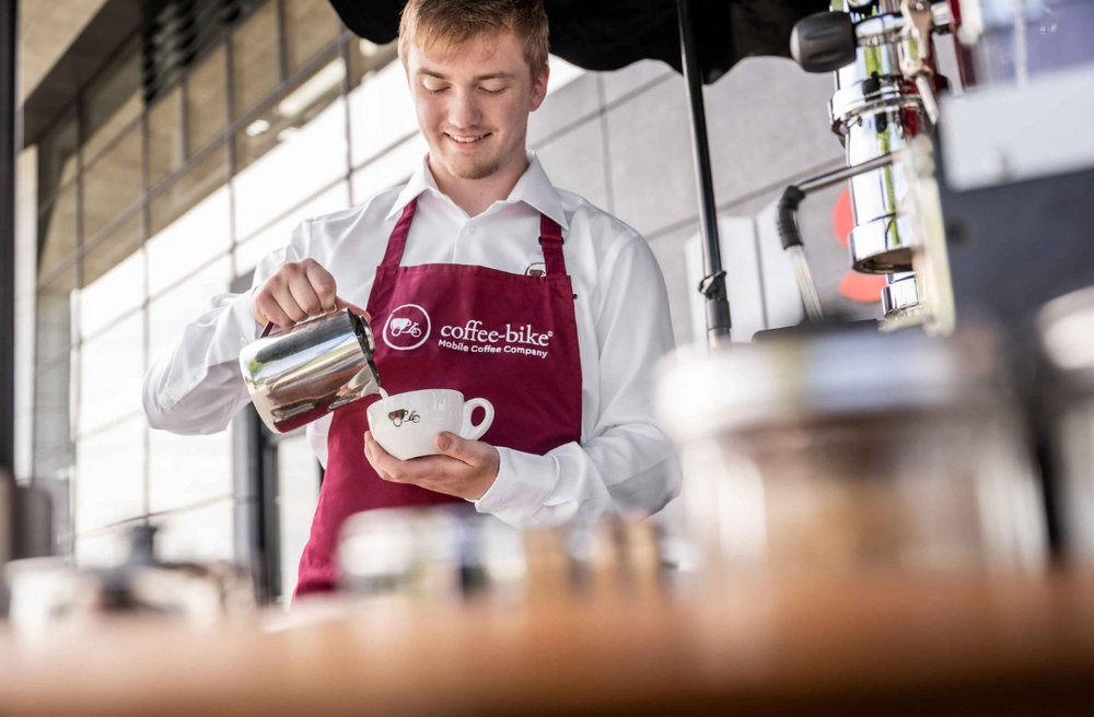Kaffeeliebhaber gießt Milch in eine Coffee-Bike Tasse ein