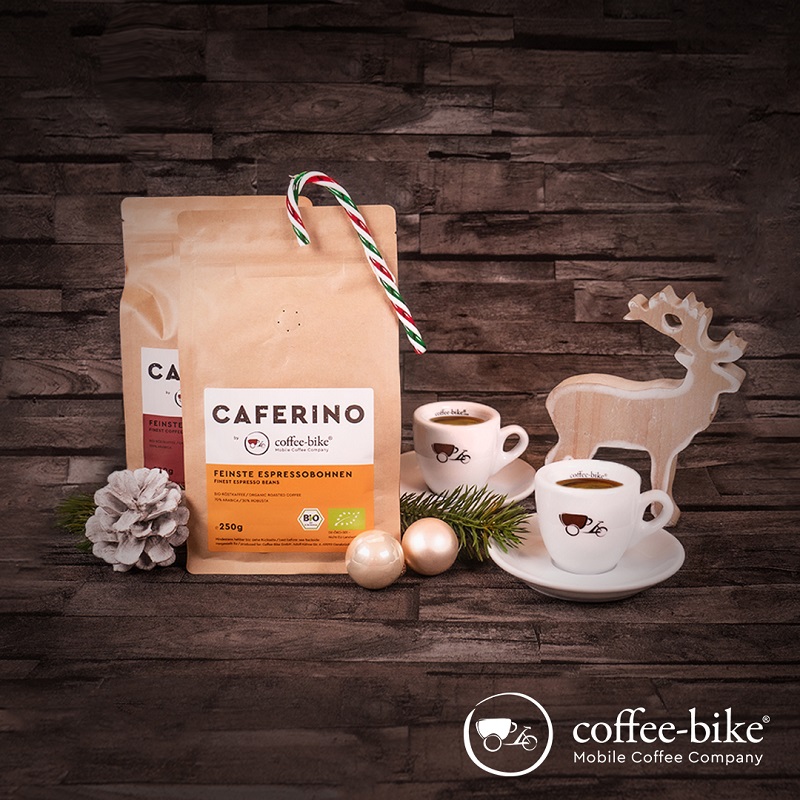On a dark background on the left are two Caferino bean packs, on one of them is a candy cane, next to it are two espresso cups, behind it is a wooden decorative reindeer, bottom right white Coffee-Bike logo
