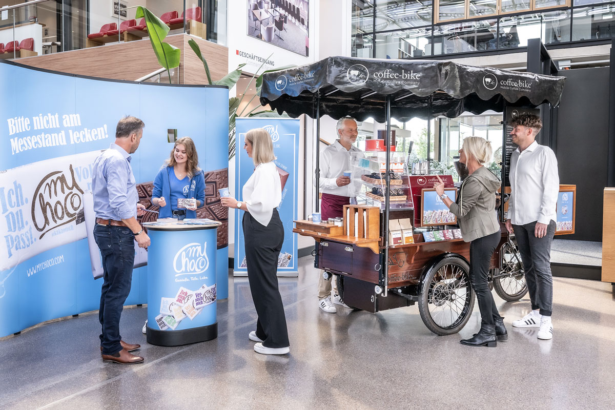 Coffee-Bike at a myChoco booth with branded posters where trade show visitors order specialty coffees and talk to the barista and promoter
