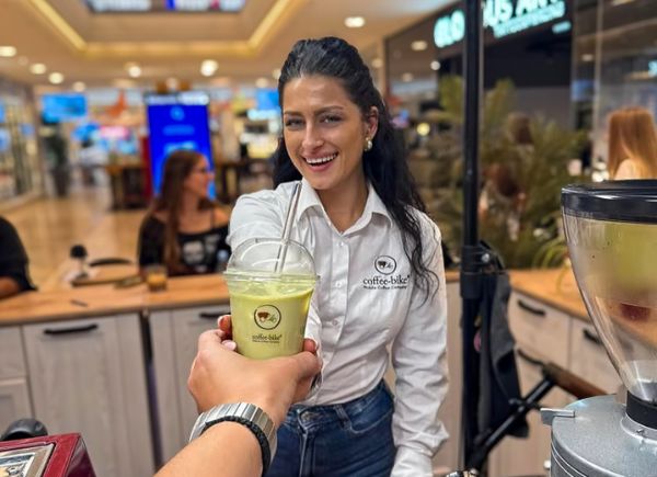 Coffee-Bikerin nimmt an ihrem Verkaufsplatz ein Iced Coffee Getränk entgegen