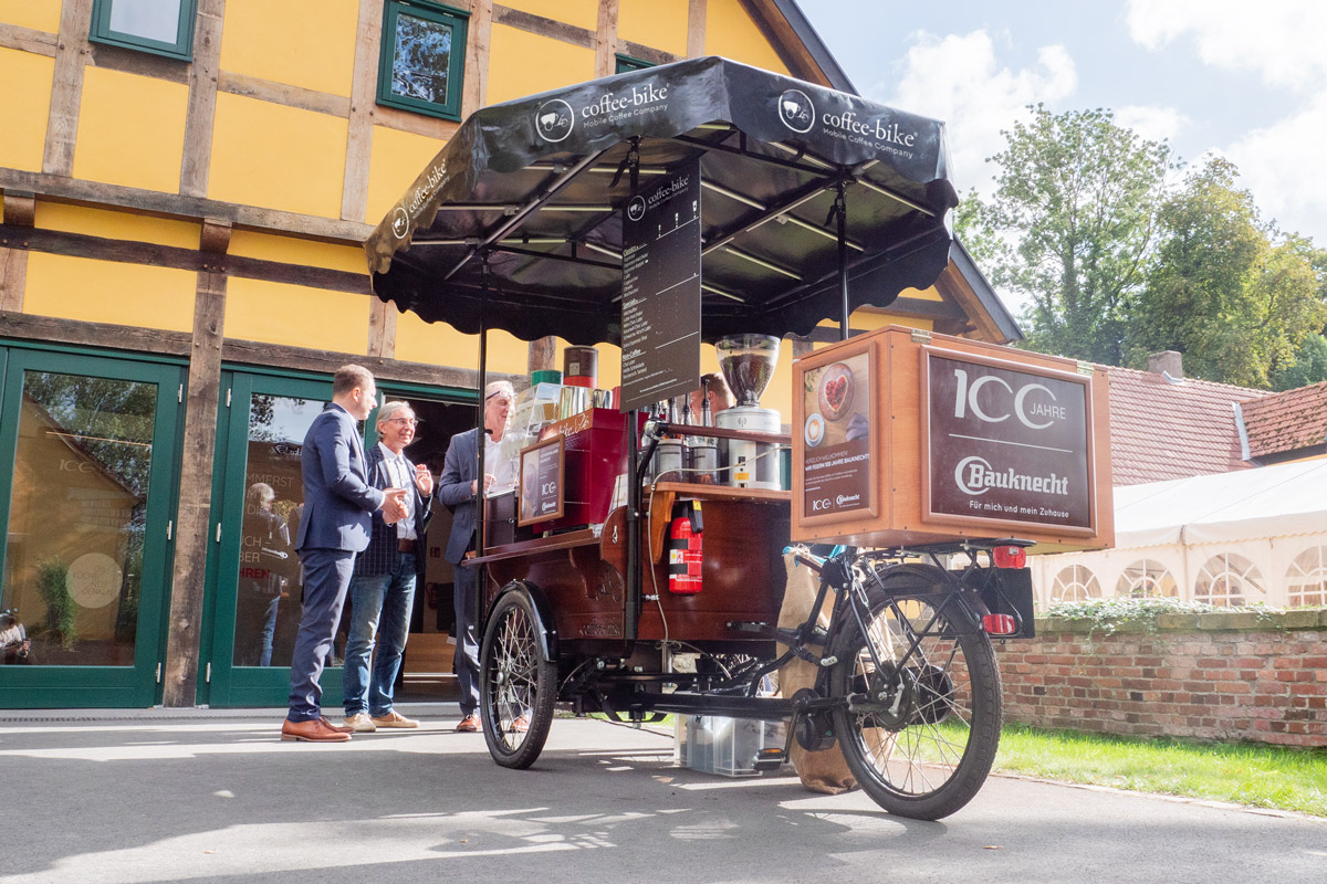 Drei Geschäftsmänner stehen am Coffee-Bike, das Bauknecht Branding zeigt